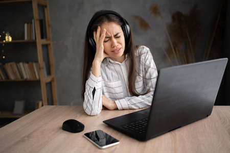 young hispanic woman having headache while working on laptop at home, stressed girl working with pcの写真素材