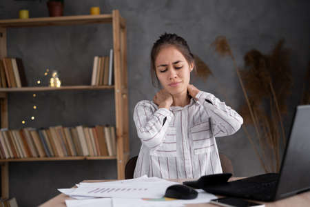 tired young woman rubbing her stiff neck massaging tense muscles, incorrect posture and sedentary work, fibromyalgia, incorrect postureの写真素材