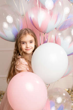 Happy celebration of birthday party with balloons of charming cute little girl in dress smiling to camera on pink background. Charming smile, expressing happiness.の写真素材