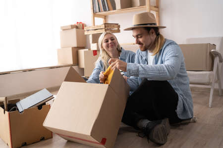 Happy young couple moving into a house, unpacking boxes while sitting in a new apartment on the floor, relocationの写真素材