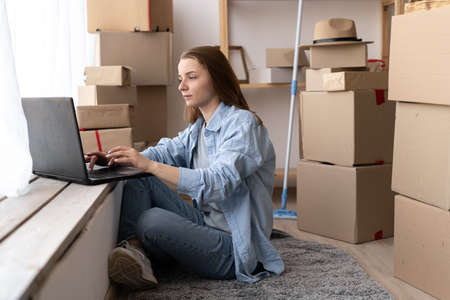 Young girl sitting on the floor using laptop computer wireless internet, moving to a new house, moving dayの写真素材