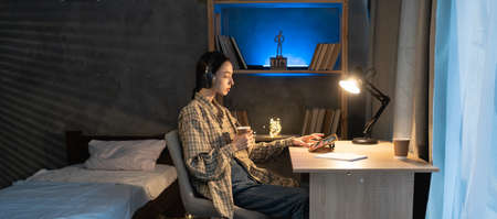 asian girl student use the digital tablet pc and headphones in the evening, watch a movie or listen to music at home at nightの写真素材