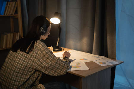 Young asian girl working think idea for project and paper having problem at night at home, female student studing using notebook with frustrated and trouble, education and freelanceの写真素材