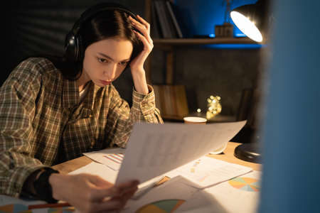 Focused asian girl young businesswoman working with papers on a project at night at home, concentrated japanese female student consider paperwork do correctionsの写真素材