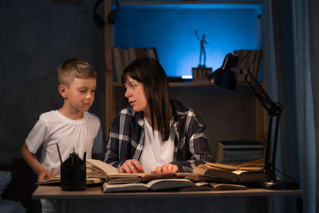 mother helping adorable son doing schoolwork at home at night, homeschoolingの写真素材