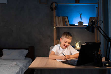 boy is doing homework using a laptop computer at his bedroom desk at nightの写真素材