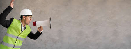 Arabic male contractor in hardhat standing with megaphone on gray background and shouting with loud and noise, engineer or foreman shouting into a bullhorn and swearing, bannerの写真素材