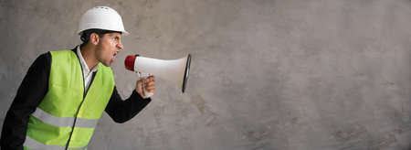 Muslim foreman shouting over grey background. Handsome happy construction worker shouting loud by megaphone with negative emotions on his face. Marketing or salesの写真素材