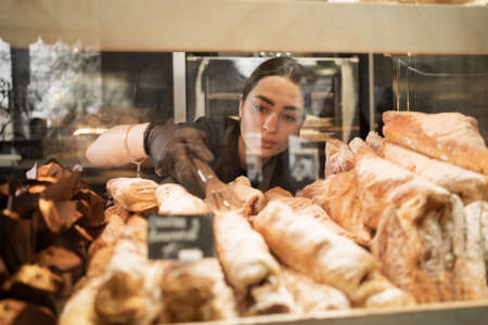 Young woman preparing pastry for sale in supermarket bakery department. Bakery seller.の写真素材