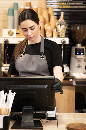 Small startup business owner. waitress girl in apron using finger touching screen of POS terminal in coffee shop. young woman staff in coffeehouse take order and print receipt in cafeの写真素材