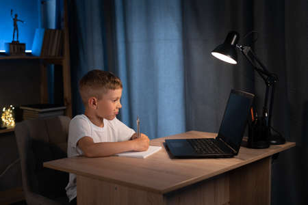 boy with drawing compass doing homework, learning at home at night using laptop for online lesson, online education and homeschoolingの写真素材