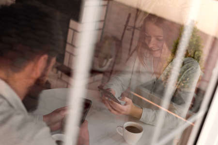 Loving couple using a mobile phone in a cafe. Reflection outside, focusの写真素材