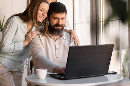 Happy young couple with laptop at home, on table at home or hotel room with windowの写真素材