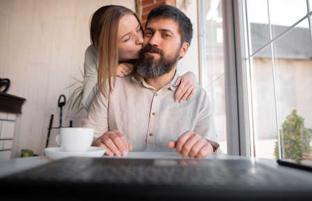Young European man and woman making video call from home, looking and speaking at webcam, wife kissing husband, smiling at camera.の写真素材