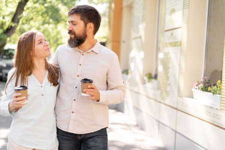 Positive young couple with takeaway coffee walk enjoying conversation while toothy smiling and looking at each other, relationship and lifestyle conceptの写真素材