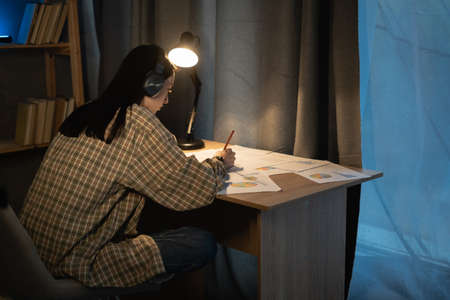Asian girl student studying at home at night, working with graphs and charts for a new project, overtime and studyの写真素材