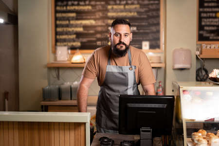Male barista at counter using cashbox computer in cafe store. Indian Waiter in apron working in coffee shop.small business, people and serviceの写真素材