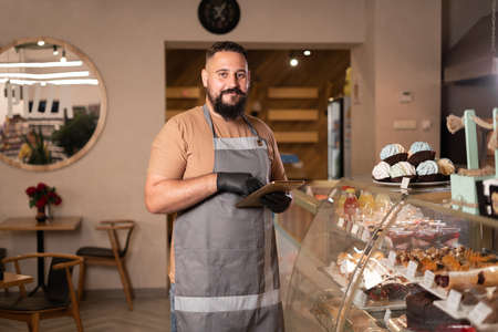 Portrait of successful young Indian cafe owner standing using digital tablet. small business owner in coffee shopの写真素材
