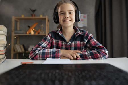 Distance E-learning. Cute teenage girl having video lesson using laptop at home, studying with computer, online education, webcam viewの写真素材