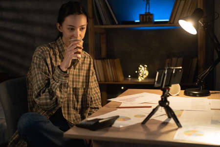 asian girl student studying late at night using smartphone at home, female student relaxing drinking coffee and preparing for examの写真素材