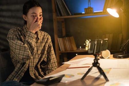 Speechless young Asian woman using smartphone at night at home opened mouth reacts to shocking news stares, female student having cyberbullying from networkの写真素材