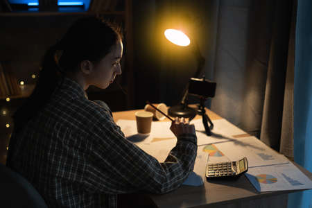 Asian student girl studying late at night at home, using a mobile phone to study online, education and school conceptの写真素材