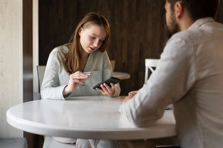 man looking at his girlfriend buying online in cafe, girl holding credit card paying for purchase in phone, cashless payment, banking and shoppingの写真素材