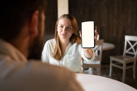 woman hands holding mock up smart phone with modern cafe background. Girl showing empty screen to his man. White screen phoneの写真素材
