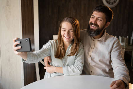 Happy young couple taking selfie, looking at camera and smiling sitting in cafeの写真素材