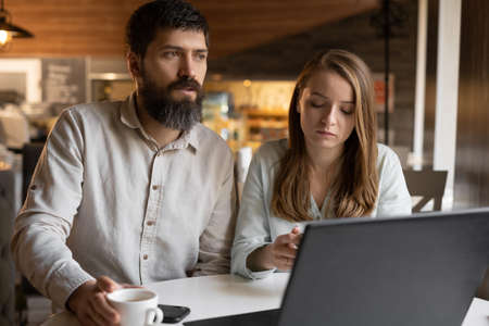 seriously couple sitting at cafe looking at laptop screen, spending time with pleasure, drinking coffee.の写真素材