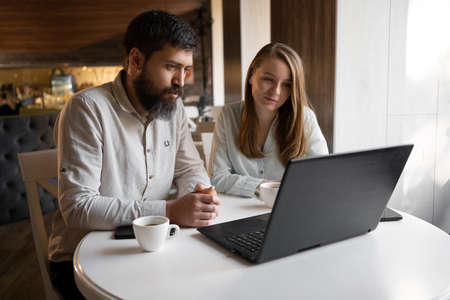 Happy young couple working in cafe using laptop, wireless internet for work, happy time together enjoyment, remote workの写真素材