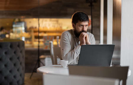 pensive bearded businessman tired of freelancer remote work relaxing in cafe, young man using laptop in coffee houseの写真素材