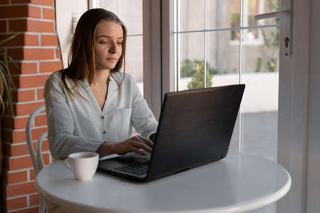 Beautiful young girl working in a cafe using a laptop, freelance business remote work, blonde female student works on notebook after lecturesの写真素材