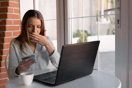 Worried woman having trouble paying online with credit card and laptop at cafe. womans hand holding credit cards, feeling stressed about debt problem from shopping online.の写真素材