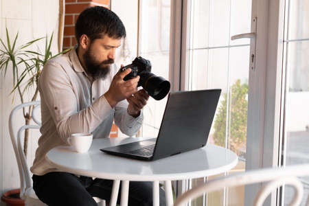 Creative Photographer working with laptop and digital camera at cafe. Professional journalist or freelancer looking at photographs with DSLR cameraの写真素材