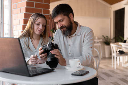 Young successful freelance photographer looking through pictures on camera while working in cafe. New modern technologiesの写真素材