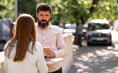 Romantic young couple drinking coffee outdoors while standing at a table in a street cafe, man and woman enjoying a relaxing conversationの写真素材