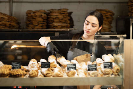 Cafe waitress girl puts fresh pastries on the cafe showcase, bakery workerの写真素材