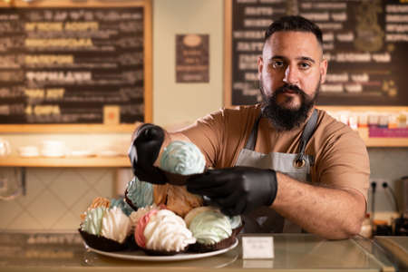 Portrait of a smiling male waiter in a cafe holding a cake and looking at the camera, barista work in a coffee shopの写真素材