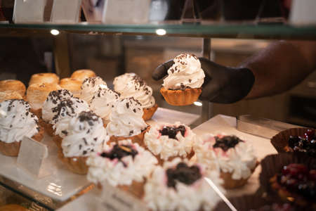 Pastry shop glass display with selection of cream cake, hand takes a cakeの写真素材