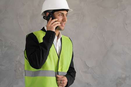 Muslim Builder with phone. Man in construction workers uniform. Repairman in vest and helmet. Foreman on grey background.の写真素材