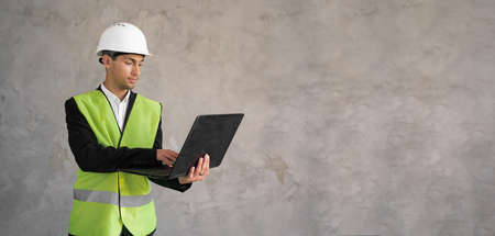 Muslim civil engineer using laptop. Engineering and construction concept. Engineer with laptop computer. Man in hard hat. Architect in yellow vest on grey background. Bannerの写真素材