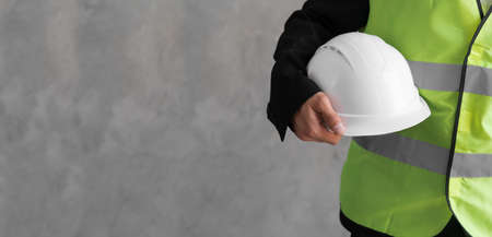 Close-up workwear and helmet in engineer or constructor hand as safety uniform isolated on grey background. Bannerの写真素材