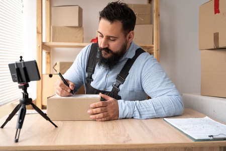 Start up. Indian man have new order from customer using mobile phone and delivery parcel box on table, small business owner working at home office, SME, shopping onlineの写真素材