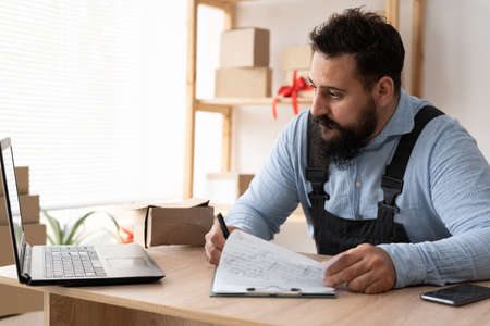 Indian male business owner sitting at home office using computer, online marketing packaging box delivery, SME e-commerce telemarketingの写真素材
