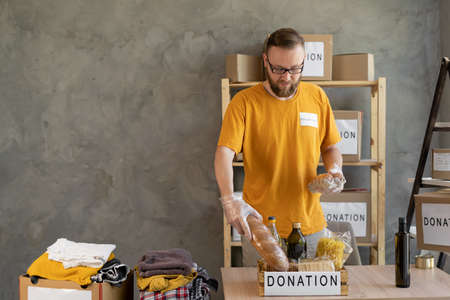 Portrait of man holding clothes donation box in office against grey background, volunteer with donations for poor people, donation box of productsの写真素材