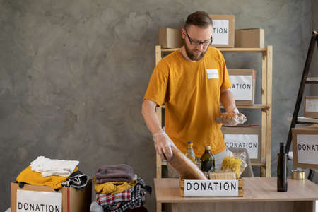 Male volunteer packing donation box with groceries and necessary things for people in need, volunteering conceptの写真素材