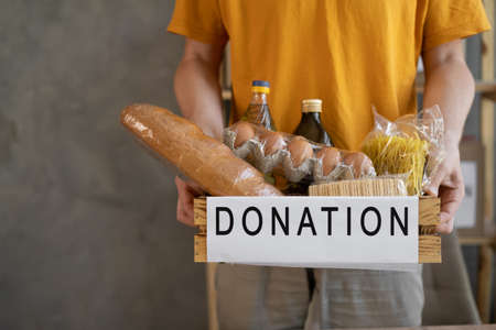 A man holding a donation box of different products on grey background, Volunteer with donations box with foodの写真素材