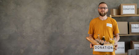 A man holding a donation box of different products on grey background, bannerの写真素材