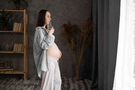pregnant woman drinking pure water from a glass at home, expectant mother takes care of babys healthの写真素材